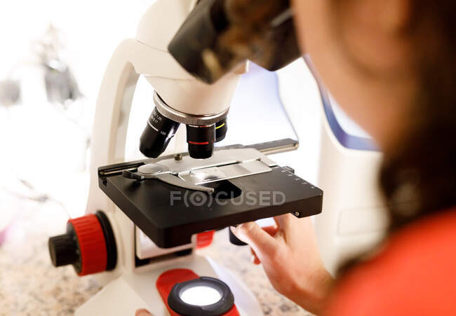 Back view of unrecognizable female doctor looking through modern microscope while at sample while working in modern clinic — Stock Photo