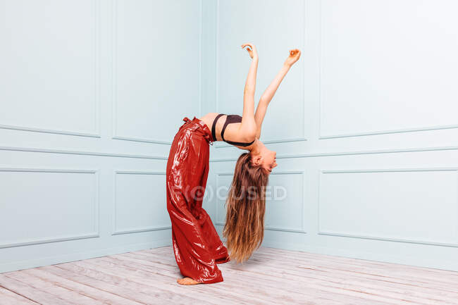 Vista lateral da fêmea fina em roupa elegante dobrando-se para trás enquanto dança no canto perto de paredes ornamentais — Fotografia de Stock