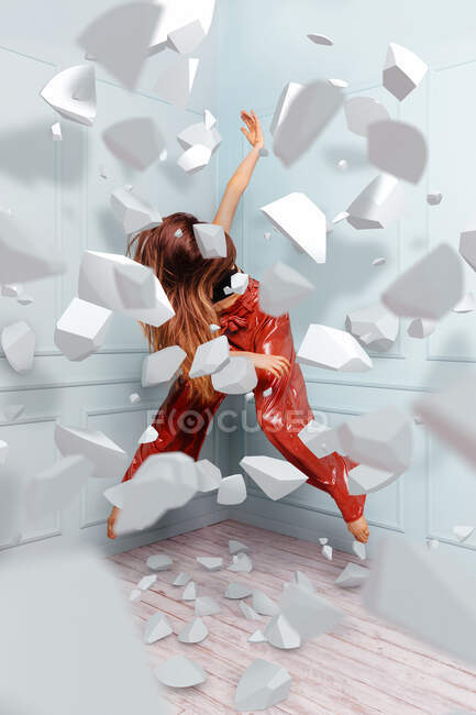 Full body anonymous energetic woman in stylish outfit jumping in corner behind falling pieces of broken wall — Stock Photo