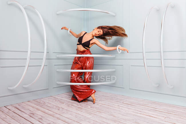 Full body slim young female in trendy outfit shaking hair and closing eyes while dancing in corner behind rings — Stock Photo