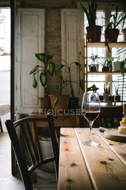 Glasses with red wine placed near cheese on wooden table in rustic restaurant with potted green plants on window — Stock Photo