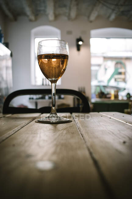 Copo de vinho colocado na mesa de tábua de madeira contra a luz do dia das janelas no restaurante rústico — Fotografia de Stock