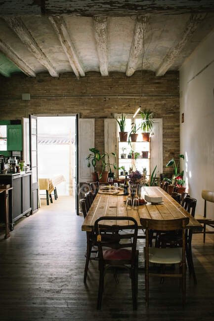 Grande table et chaises en bois dans un bar rustique de style rétro avec plafond minable et plantes vertes en pot sur la fenêtre — Photo de stock