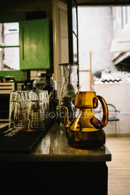 Jarras de vidrio anticuadas con bebidas colocadas en el mostrador cerca de vasos limpios en un pub rústico - foto de stock