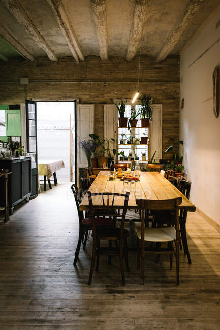 Großer Holztisch und Stühle in rustikalem Retro-Stil mit schäbiger Decke und grünen Topfpflanzen am Fenster — Stockfoto