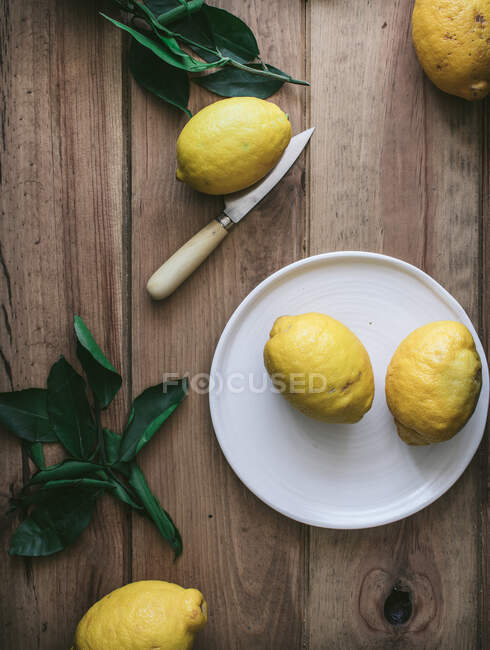 Draufsicht auf geschälte und frische Zitronen auf Tellern auf Holztisch mit grünen Blättern — Stockfoto