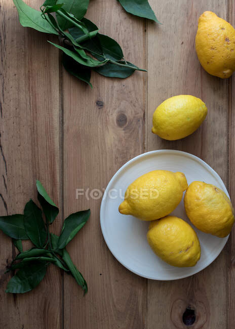 Вид зверху очищені і свіжі лимони на тарілках на дерев'яному столі з зеленим листям — стокове фото