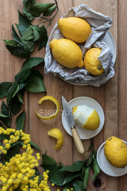 Top view of peeled and fresh lemons on plates on wooden table with green leaves and yellow flowers — Stock Photo
