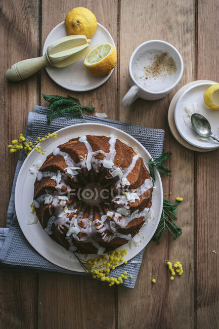 Draufsicht von oben leckerer frischer veganer Kuchen mit Zitrone und Kokosnuss überzogen mit Glasur auf Holztisch mit Zutaten — Stockfoto