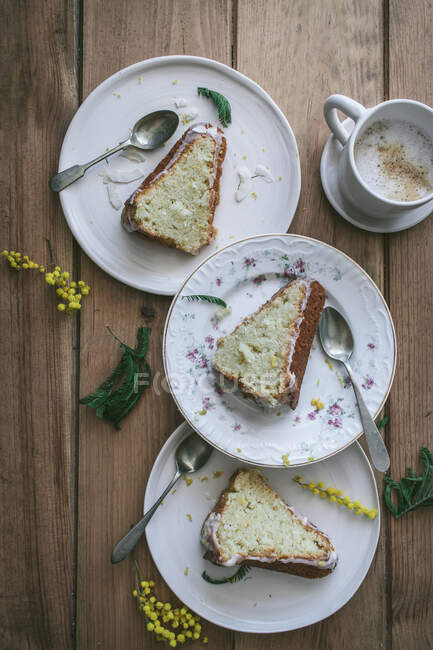 Верхній вигляд шматочків свіжого веганського лимона і кокосового торта на тарілках з ложками і чашкою кави. — стокове фото