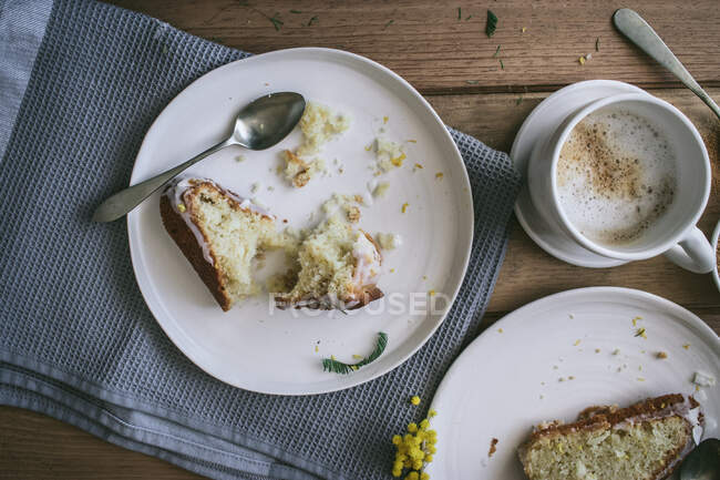 Draufsicht auf Scheiben frischen veganen Zitronen- und Kokoskuchens auf Tellern mit Löffeln und Tasse Kaffee — Stockfoto