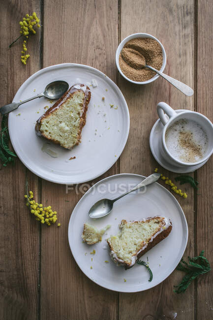Vista dall'alto di fette di limone vegano fresco e torta di cocco su piatti con cucchiai e tazza di caffè — Foto stock