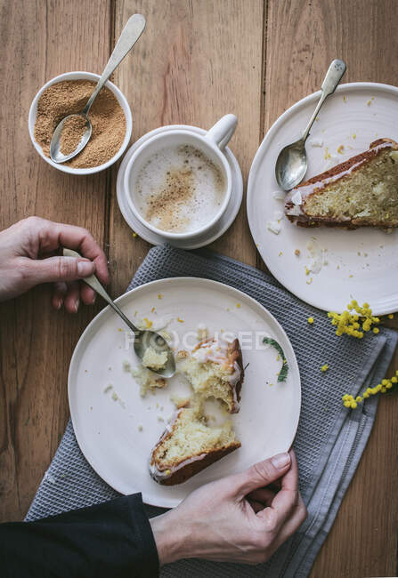 Вид зверху на безлику леді тримає тарілку з шматочком торта за дерев'яним столом зі смачними шматочками веганського лимона та кокосового пирога під час сніданку — стокове фото