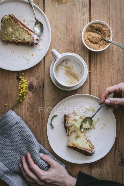 Вид зверху на безлику леді тримає тарілку з шматочком торта за дерев'яним столом зі смачними шматочками веганського лимона та кокосового пирога під час сніданку — стокове фото