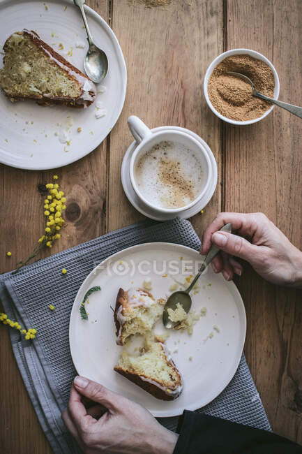 Вид на безликую даму, держащую тарелку с кусочком торта за деревянным столом с вкусными кусочками веганского лимона и кокосового пирога во время завтрака — стоковое фото