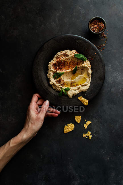 Top view of unrecognizable person hand holding stylish black plate with delicious fresh eggplant and cauliflower dip stylish decorated with colorful spices and leaves of mint — Stock Photo