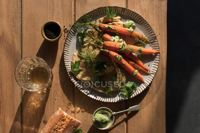 Top view of slices of fresh bread spread with hummus on plate with baked orange carrots decorated with green sauce on wooden table — Stock Photo