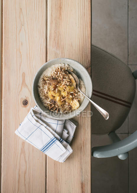 Vista superior da tigela com mingau de cereal fresco servido com fatias de banana e colher na mesa de madeira — Fotografia de Stock
