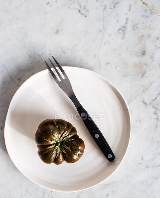 Vista superior de grandes tomates verdes inmaduros en plato negro con tenedor de metal y trozo de queso en plato - foto de stock