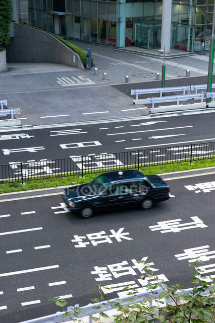 Над сучасним чорним автомобілем, що їде по безлюдній асфальтній дорозі з маркуванням та ієрогліфами на вулицях міста в Японії. — стокове фото