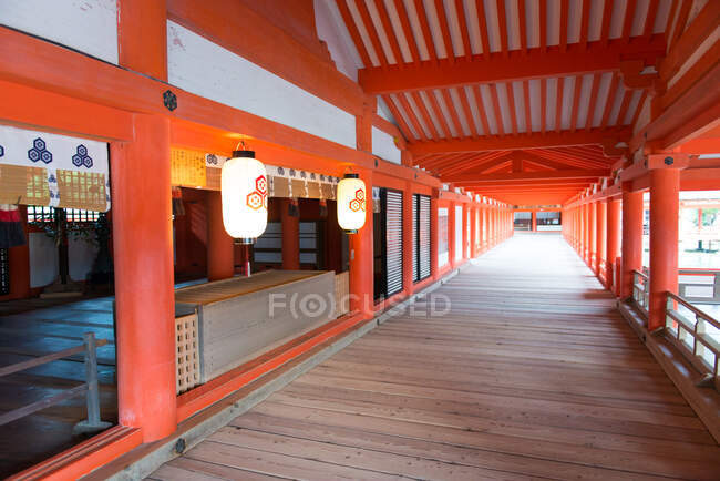 Empty covered passage with wooden floor and red columns with traditional lanterns in floating Shinto shrine in Japan — Stock Photo