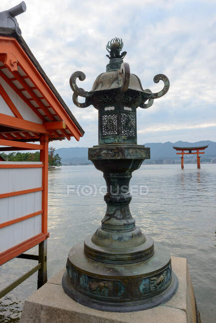 Hermosa escultura de piedra envejecida junto al agua con puerta flotante en el fondo en el santuario de Itsukushima en Japón - foto de stock