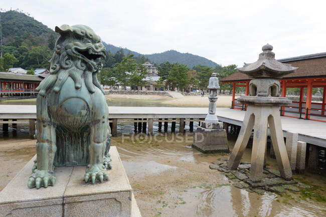 Statue en bronze de chien lion gardien traditionnel situé dans le sanctuaire shinto au Japon avec des collines verdoyantes et un ciel nuageux en arrière-plan — Photo de stock