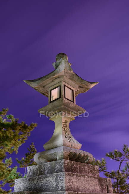 From below of beautiful illuminated ancient stone sculpture in oriental style against purple night sky — Stock Photo
