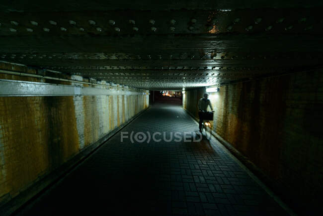 Persona irriconoscibile in sella alla bicicletta nel passaggio sotterraneo buio con pareti intemperie di notte in città in Giappone — Foto stock