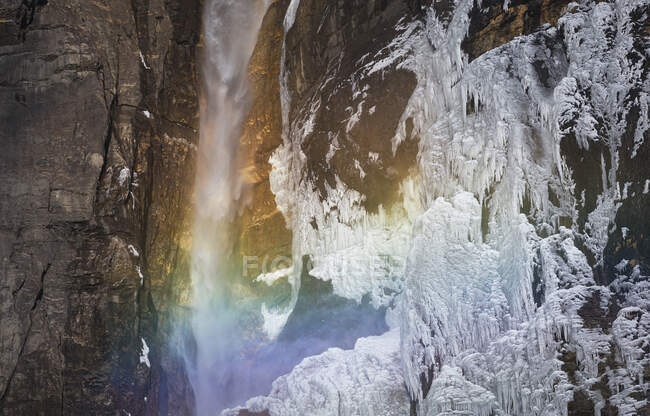 Cenário incrível com arco-íris em pequena cachoeira caindo de penhasco e parede rochosa congelada no campo canadense — Fotografia de Stock
