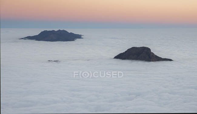 From above peaks of rocky mountains over thick white clouds with pink sunrise sky in background in Iceland — Stock Photo