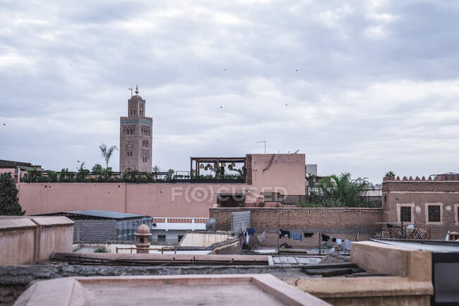 Edificios Shabby y antiguo minarete situado en la calle de la ciudad árabe contra el cielo nublado - foto de stock