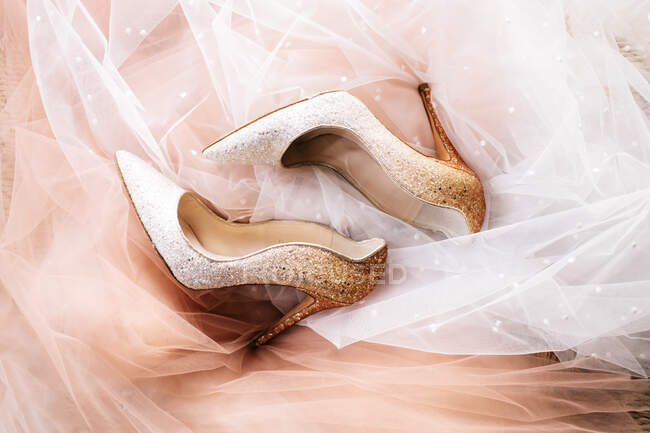 Vue de dessus de chaussures stiletto scintillantes placées sur un tissu voile rose et blanc avec des paillettes — Photo de stock