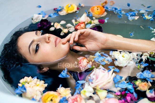 D'en haut attrayant visage féminin tout en étant couché dans la baignoire avec de l'eau chaude et diverses fleurs colorées — Photo de stock