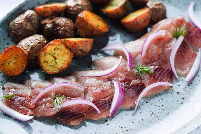 Von oben Stücke von leckeren Bratkartoffeln in der Nähe von marinierten Fischscheiben mit frischen Zwiebeln und Dill auf Teller im Café platziert — Stockfoto