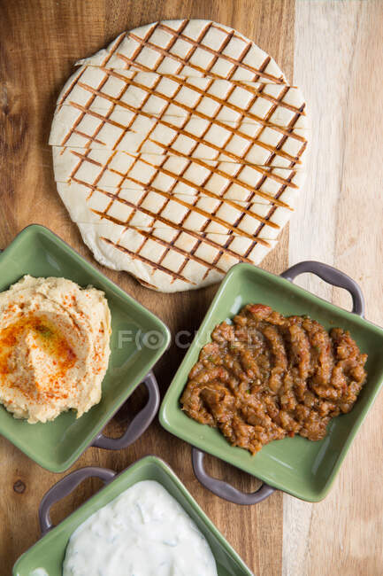 Верхний вид тарелок с разнообразными соусами, поставленных на деревянный стол рядом с нарезанной жареной тортильей в кафе — стоковое фото