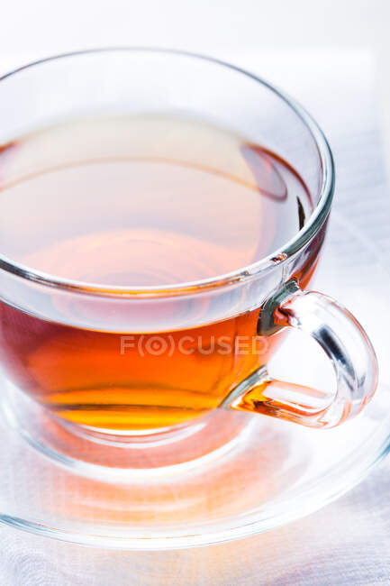 Primer plano de la taza de vidrio de té caliente aromático colocado en platillo en la mesa en la cafetería - foto de stock