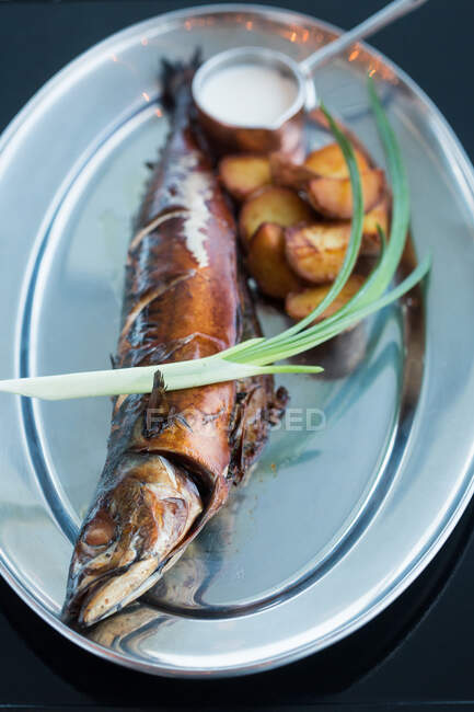 From above delectable fried fish and potatoes with fresh scallion and cream sauce placed on metal plate in restaurant — Stock Photo