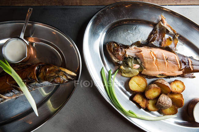 Top view of yummy roasted fish and potatoes served with ripe scallion and cream sauce on metal plate in restaurant — Stock Photo