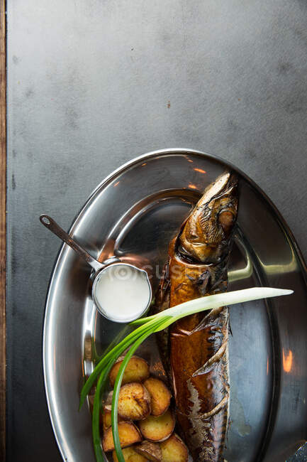 Вид зверху смачної смаженої риби та картоплі, яку подають зі стиглою цибулею та вершковим соусом на металевій тарілці в ресторані — стокове фото