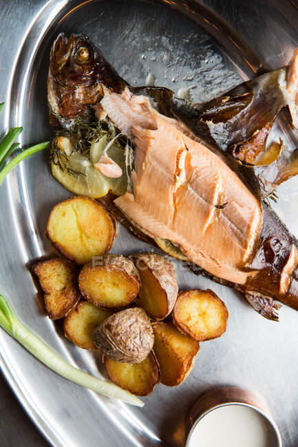 Vista superior do delicioso peixe assado e batatas servidas com cebolinha madura e molho de creme em placa de metal no restaurante — Fotografia de Stock