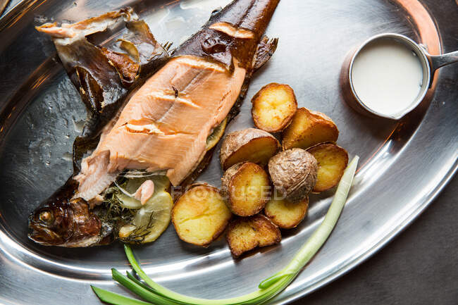 Вид зверху смачної смаженої риби та картоплі, яку подають зі стиглою цибулею та вершковим соусом на металевій тарілці в ресторані — стокове фото