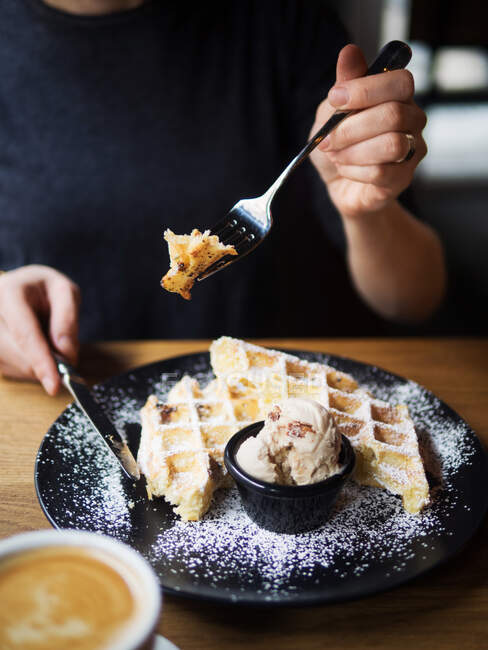 Unbekannter schneidet mit Form und Messer süße Waffeln in der Nähe von Schüssel mit Eis und Tasse Kaffee auf Tisch im Café — Stockfoto