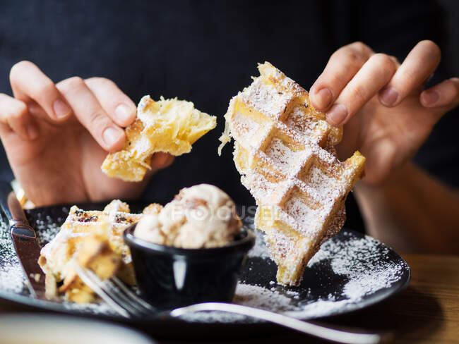 Persona anonima rompere pezzo di cialda morbida sul piatto con gustoso gelato mentre seduto a tavola nel ristorante — Foto stock