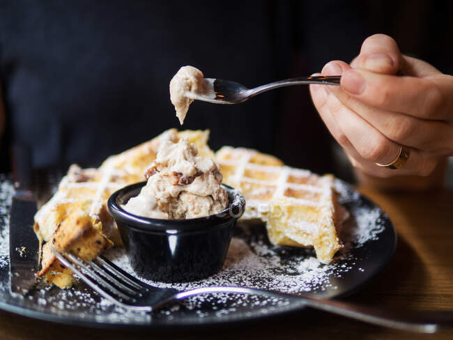 Неузнаваемый человек, наслаждающийся холодным сладким мороженым и свежими вафлями во время обеда в кафе — стоковое фото
