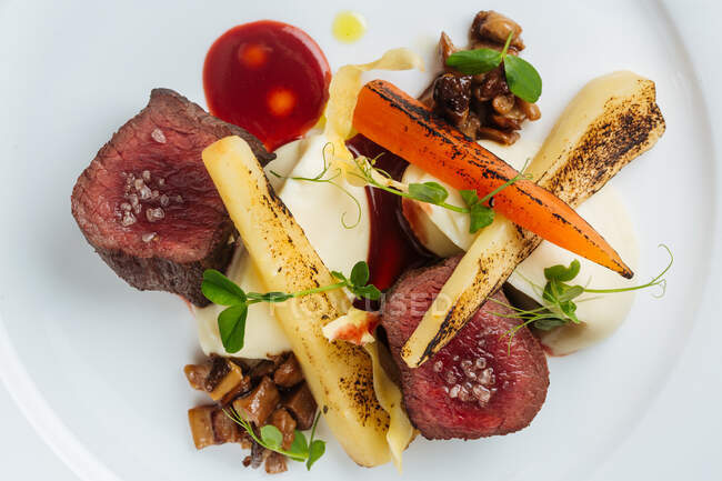 Blick von oben auf köstliche Gourmet-Steaks mit gebratenem Fleisch und gegrilltem Gemüse, garniert mit frischen Kräutern und Sauce auf weißem Teller — Stockfoto