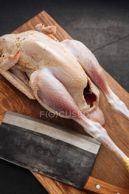 From above shabby cleaver and raw whole chicken placed on wooden cutting board in kitchen — Stock Photo