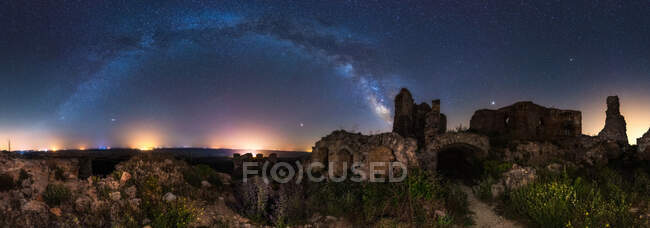 Aged ruined building among green field plants under colorful starry night sky with milky way — Stock Photo
