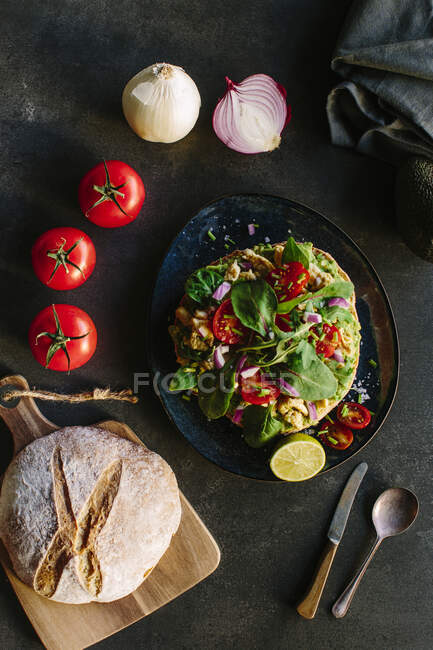 Вид зверху на різноманітні овочі та хліб, розміщені біля тарілки з смачним гуакамоле на кухні — стокове фото