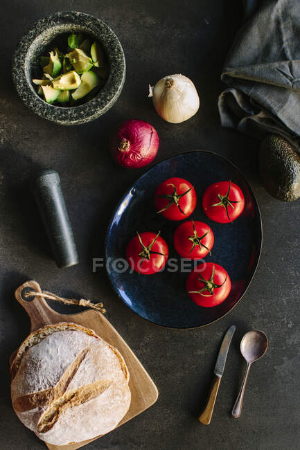 Вид зверху на різноманітні овочі та хліб, розміщені біля тарілки з смачним гуакамоле на кухні — стокове фото